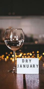 A wine glass filled with water sits next to a small marquis sign that reads Dry January
