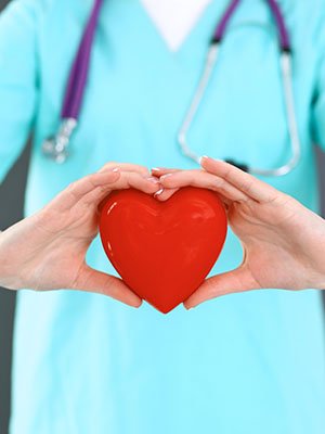 a doctor in blue scrubs holds a red valentine heart in their hands