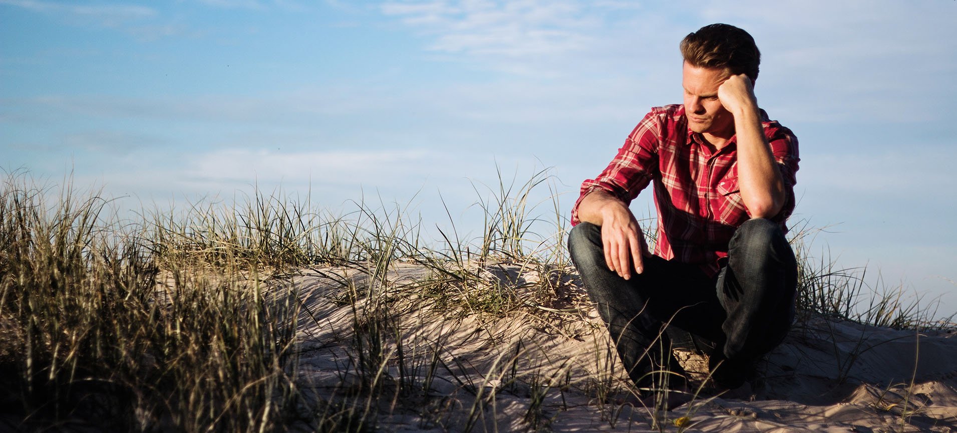 a sad man sitting on a beach dune