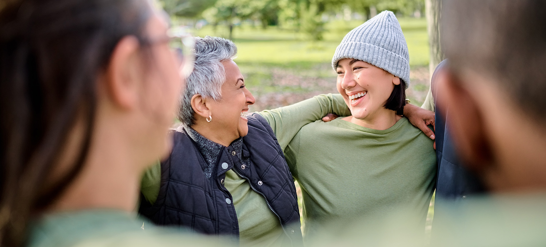 two smiling women wearing green hug shoulders in a circle