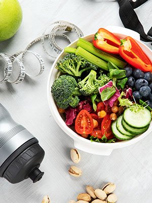 a bowl filled with colorful vegetables sits on a table with pistachios, a reusable water bottle, a tape measure
