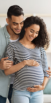a smiling man hugs a smiling pregnant woman